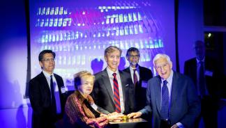 A group of people standing at a podium with a gold button. People include, from left to right, Ramanan Raghavendran, Diana Vagelos, Jeffrey Kallberg, Roy Vagelos, Vijay Kumar, and Larry Jameson.